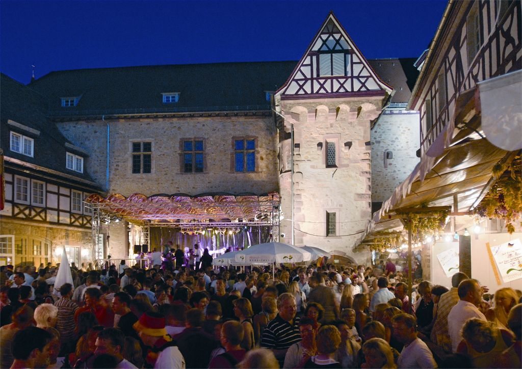 Weinmarkt Menschenmasse im Hof eines Gebäudekomplexes in U-Form bei Nacht.