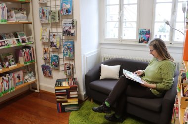 Frau ließt Buch auf Sofa neben Bücherregal